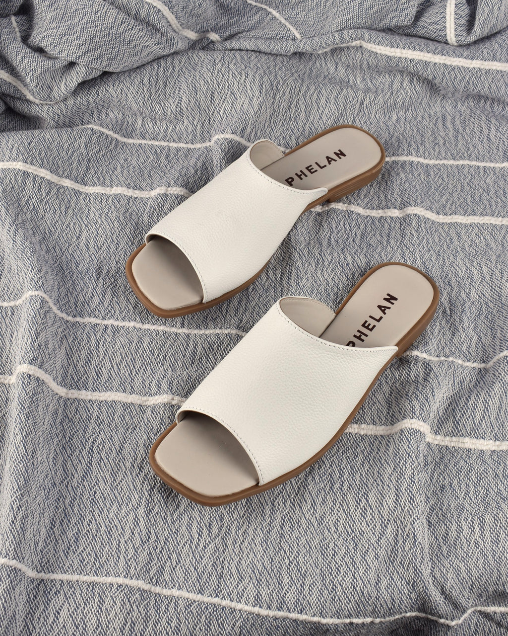 Mykonos Slide in White on a blue-grey striped throw