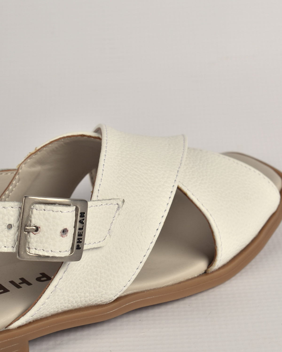 Close-up of the Capri Sandal's PHELAN buckle and pebbled white nappa