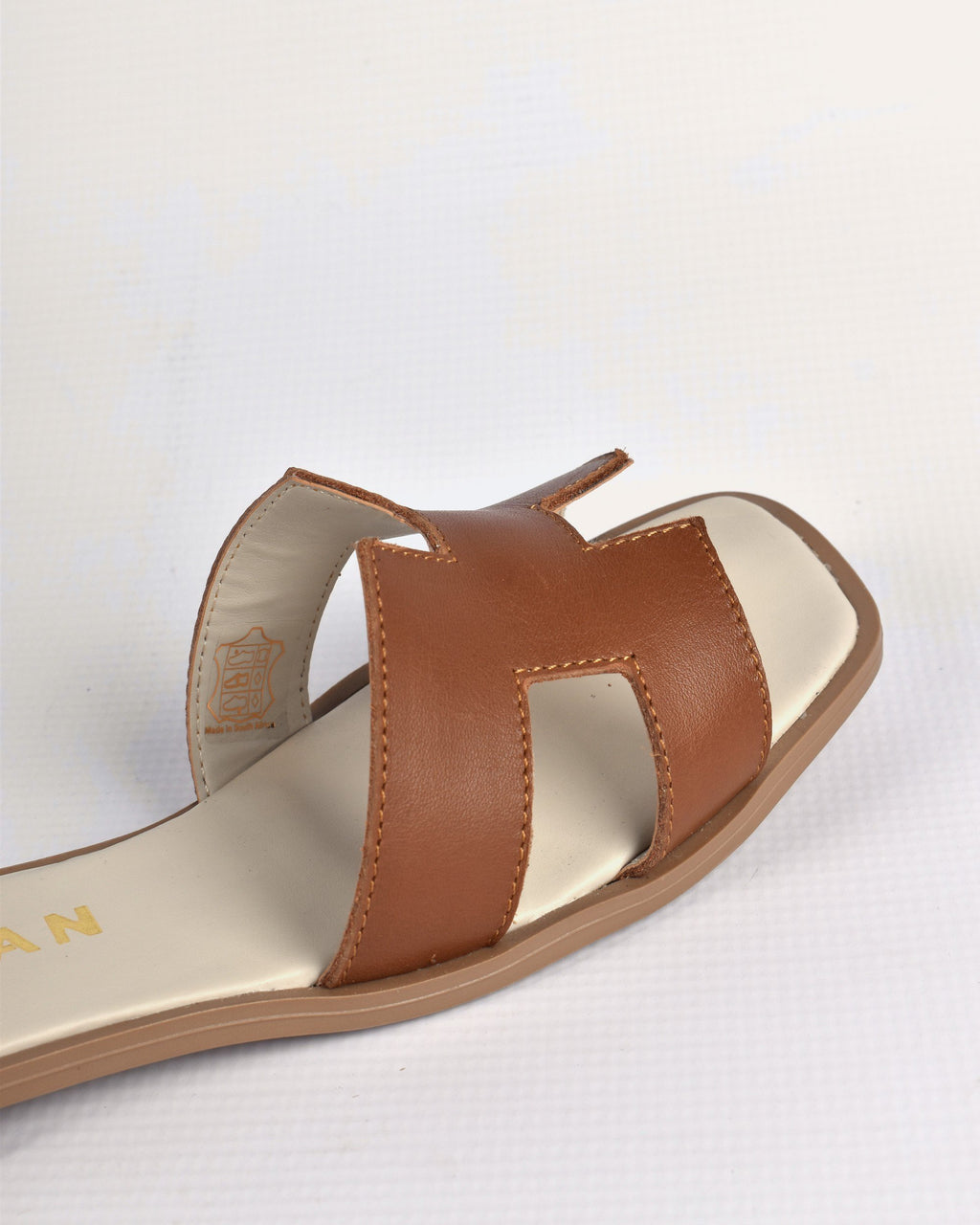 Close-up of the Santorini Slide's tan leather H strap and hand stitching