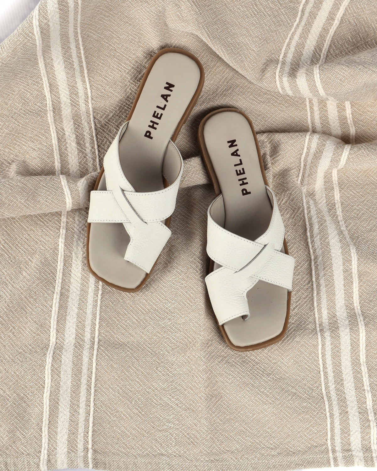 Isla Slide in White, the pair on an oatmeal throw