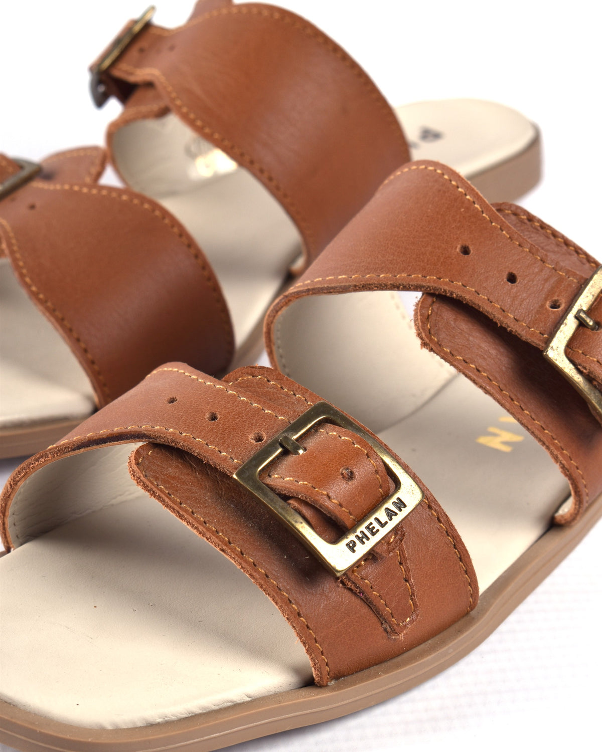 Close-up of the PHELAN brass buckle on the tan leather Buckle Sandal