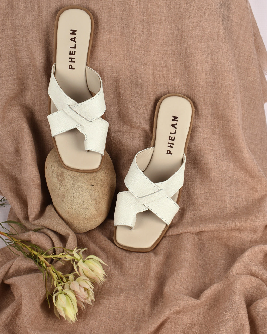Isla Slide in White, the pair on a camel throw with a stone and a protea