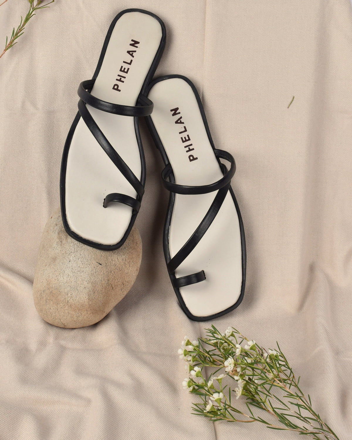 Lipari Slide in Black, the pair on an oatmeal throw with a stone and fynbos