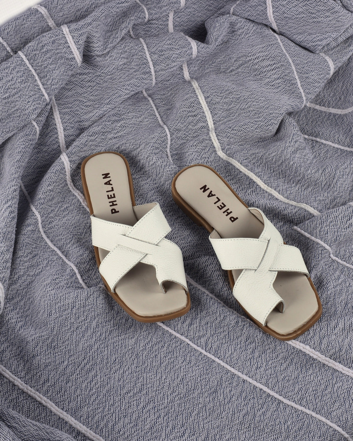 Isla Slide in White, the pair on a blue-grey throw