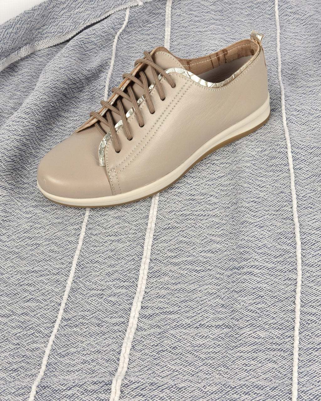Hydra Sneaker in Taupe/Gold on a blue-grey striped throw