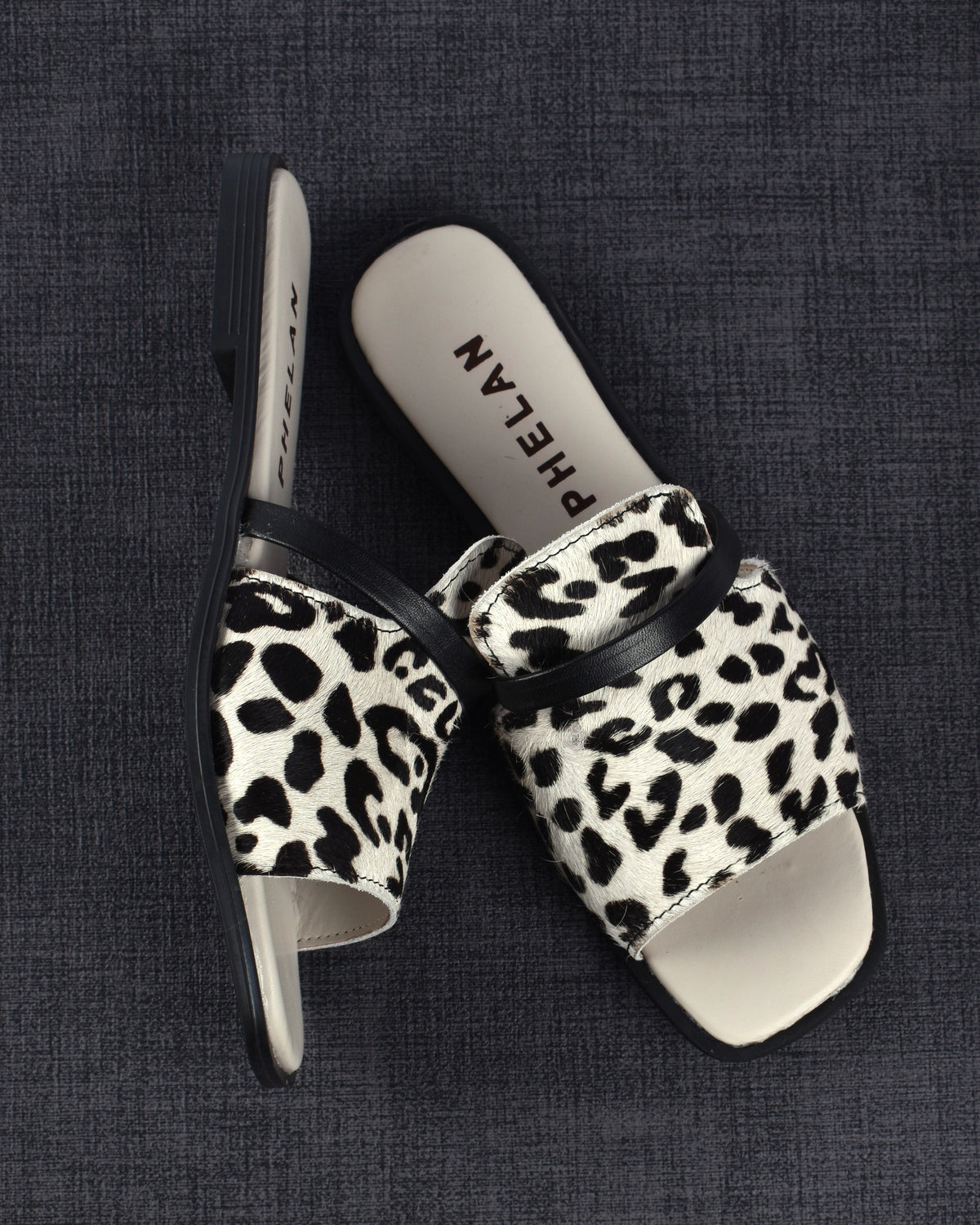 Sabi Slide pair on a charcoal linen mat, one shoe tipped on its side